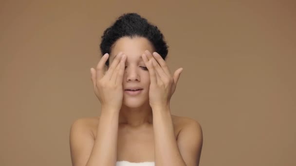 Beauty portret van jonge Afro-Amerikaanse vrouw slaan gezicht met vingers en het geven van zachte huidmassage. Zwart vrouwtje poserend op bruine studio achtergrond. Slow motion klaar, 4K bij 59,94fps. - Video