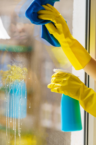 Female hand in yellow gloves cleaning window pane with rag and spray detergent. Cleaning concept - Foto, Bild