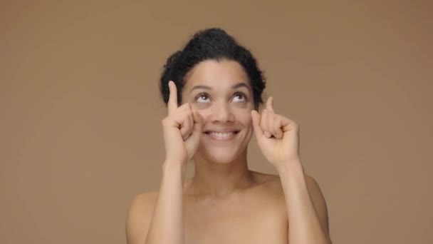 Beauty portrait of young African American woman pointing up hand for something then nods and shows thumb up. Black female posing on brown studio background. Slow motion ready, 4K at 59.94fps - Video, Çekim