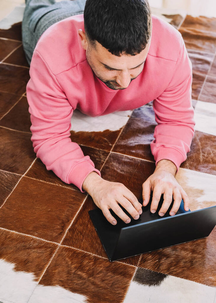 Empleado que trabaja acostado en la alfombra en su sala de estar con su computadora portátil debido a la pandemia de coronavirus - Foto, Imagen