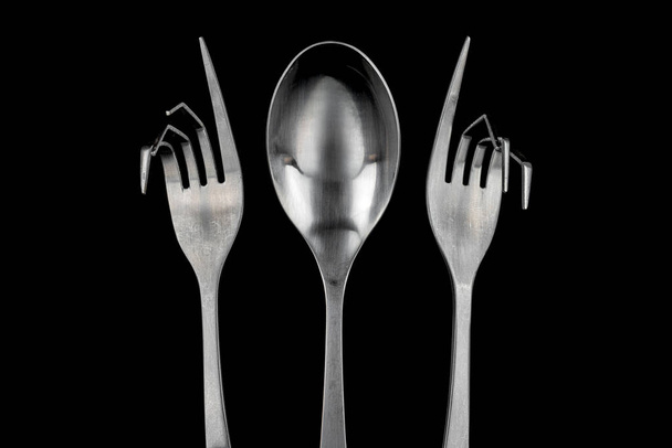 Figura conceptual de una cuchara de acero inoxidable y dos horquillas curvas de acero inoxidable sobre un fondo negro - Foto, imagen