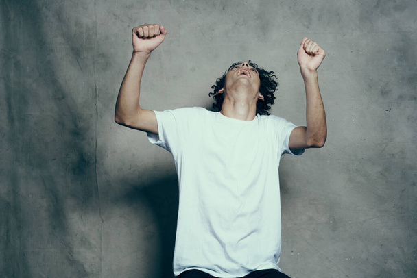 счастливый кудрявый парень в футболке жестикулирует руками на тканевом фоне в студийной фотомодели - Фото, изображение