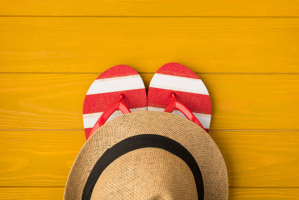 Sarı ahşap arka planda izole edilmiş parmak arası terlik ve güneş şapkası fotoğrafı. - Fotoğraf, Görsel