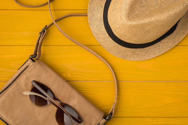 Fénykép felett napszemüveg bőr táska és sunhat elszigetelt a sárga fa háttér - Fotó, kép