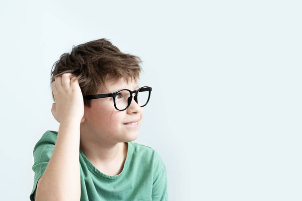 Surprised scratch boy in a green T-shirt and glasses pensive scratches his head. Copy space - Photo, Image