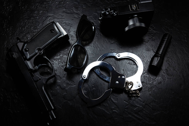 ブラックガン、懐中電灯、メガネ、カメラ、警察の金属本物の手錠は黒の背景にあります。私立探偵事務所。情報を探してる。犯罪と強盗刑務所の概念. - 写真・画像