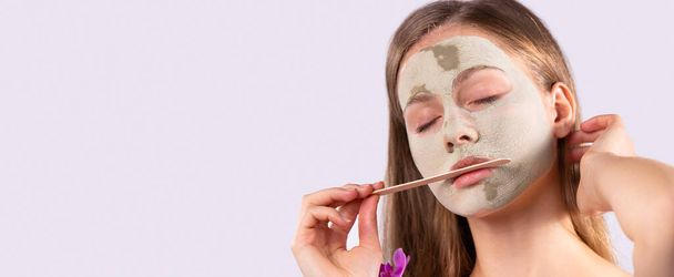 Banner, long format on gray background. Skincare. Spa beauty wellness. Young blonde charming woman take care of skin using facial mask. Side space for ad info text. High quality photo - Foto, Bild