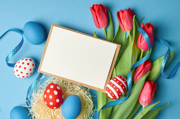 Easter holiday card mockup with colored eggs, ribbons and red tulip flowers on blue - Valokuva, kuva