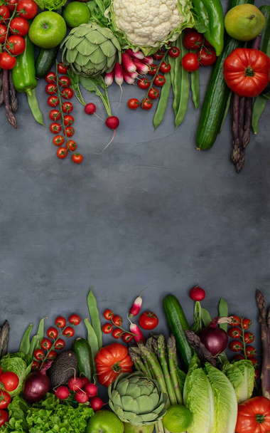 Different organic vegetables - asparagus, tomatoes cherry, avocado, artichoke, pepper, lime, lemon, salt on gray background. Raw vegan vegetarian concept. - Foto, imagen