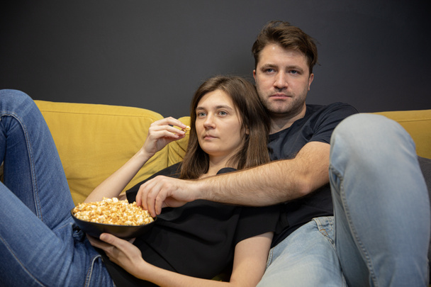 unemotional couple hugging lying on couch with popcorn in hands and watching TV - Photo, Image
