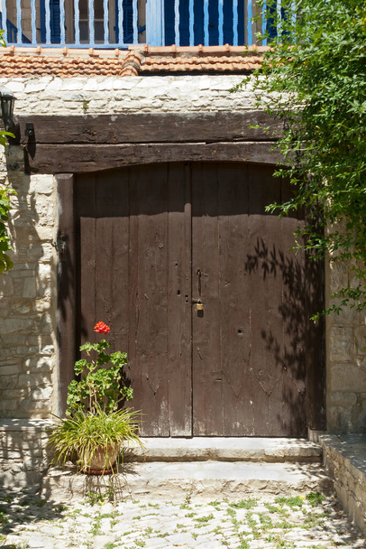 Запертая старомодная коричневая деревянная входная дверь традиционного каменного дома в деревне - Фото, изображение