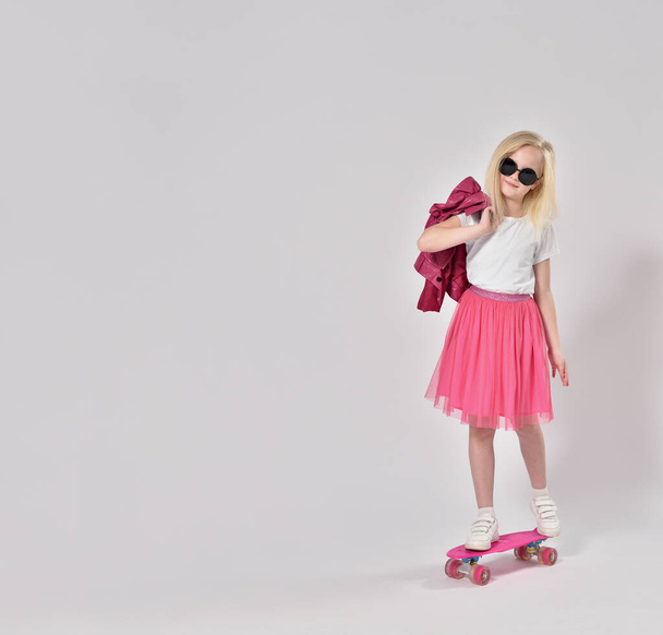 Teenage girl in pink clothes stands on skateboard - Zdjęcie, obraz
