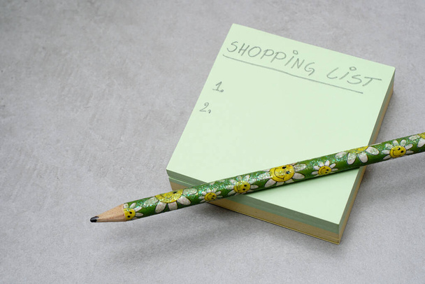 Uma lista de compras manuscrita em A Post-it Sticky Notes. Padrão de memo de forma quadrada verde.Contexto cinzento. Conceito de planejamento de compras. - Foto, Imagem