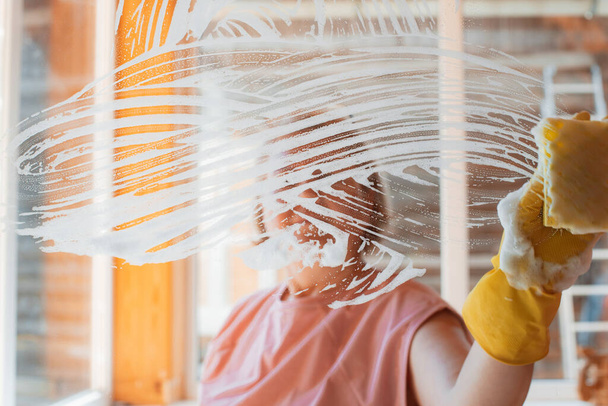 женщина делает домашнюю работу дома, моет поверхности зеркал и окон с помощью брызг моющего средства с пеной губки. - Фото, изображение