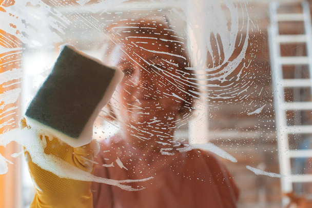 woman does household chores at home, washing the surfaces of mirrors and windows with a spray of detergent with a foam sponge. - Fotoğraf, Görsel