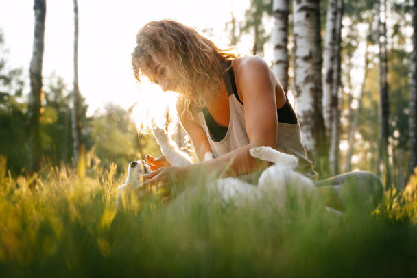 A young girl plays with a dog in the grass during sunset. - Foto, imagen