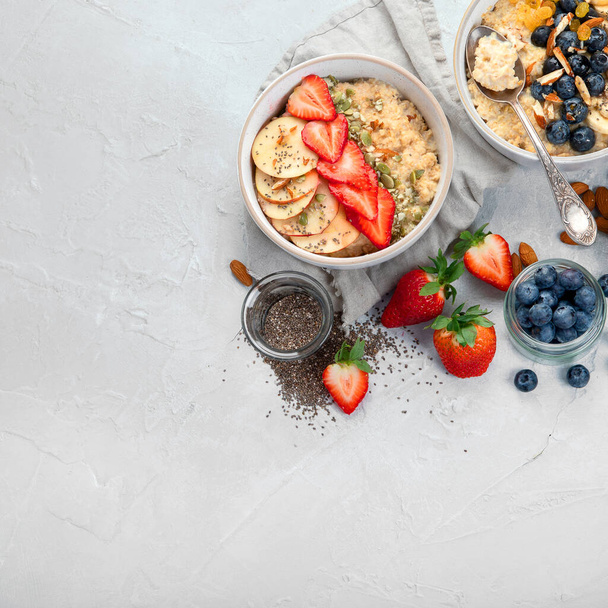 Oatmeal bowls with delicious fruits and fresh berries on light background. Healthy breakfast concept. Top view, copy space - Fotó, kép