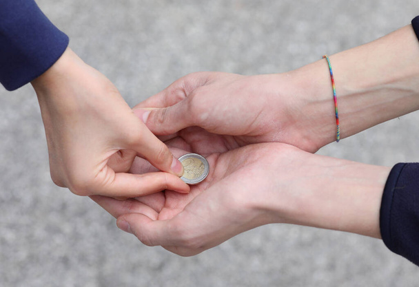 la mano de la joven mujer mientras da limosna con una moneda al pobre niño - Foto, imagen