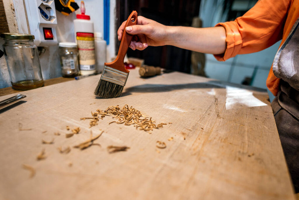 Kobieta lutnica czyszcząca wióry drewna ze stołu roboczego w tradycyjnym warsztacie. - Zdjęcie, obraz