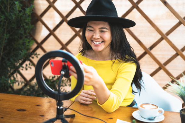 Onnellinen aasialainen nainen vlogging verkossa älypuhelimen kamera ja vaikuttaja johti juodessaan kahvia istuu baarissa - Valokuva, kuva