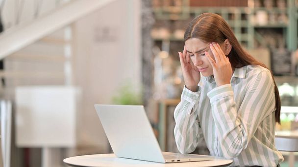 Gestresste junge Latino-Frau mit Laptop mit Kopfschmerzen im Café  - Foto, Bild