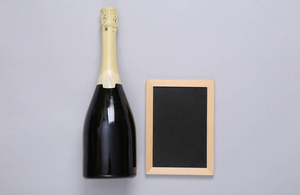 Bottle of champagne or wine with empty chalk board on gray background. Copy space - Foto, imagen