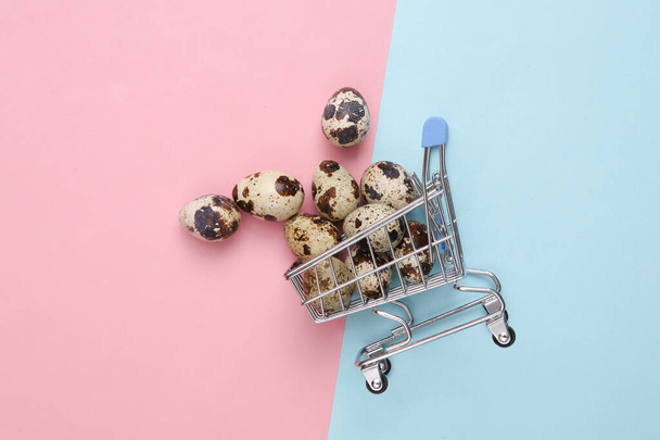 Mini supermarket cart with quail eggs on pink blue background. - Foto, Bild