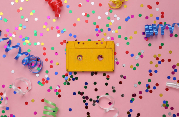 Audio cassette and colored streamer with confetti on a pink background. Music day - Foto, afbeelding