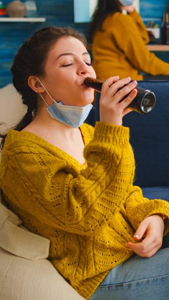 Relaxed woman taking off face mask looking at camera drinking beer - Foto, Bild