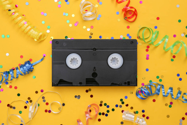 Videocassette en gekleurde streamer met confetti op gele achtergrond. Filmdag - Foto, afbeelding