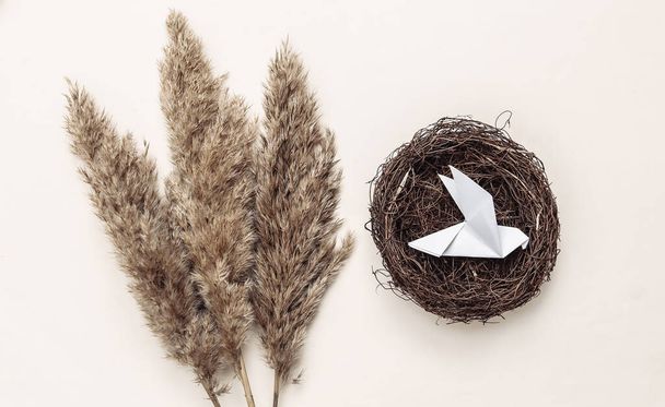 Syksyn kasviston koostumus. Pesä origami lintu, oksat ruoko on pastelli beige tausta - Valokuva, kuva