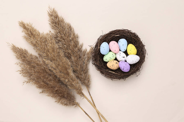Σύνθεση του Πάσχα από μια φωλιά με χρωματιστά αυγά ορτυκιού, κλαδιά καλάμι σε παστέλ μπεζ φόντο. Φυσική επίπεδη ωοτοκία - Φωτογραφία, εικόνα