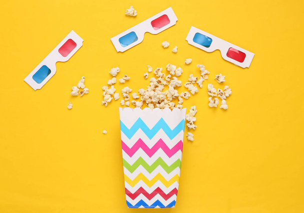 Popcorn-Eimer und 3D-Brille auf gelbem Hintergrund. Ansicht von oben. Flache Lage - Foto, Bild