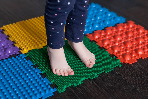 Egy kisgyerek lábai az ortopéd szőnyegen. Fényes felületek a gyalogláshoz és a láb megfelelő ívének kialakításához. Masszázs puzzle szőnyeg. - Fotó, kép