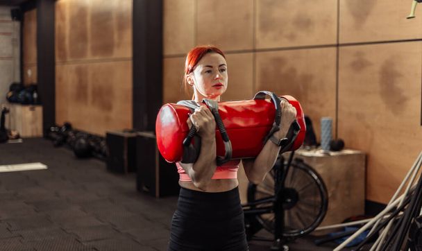 Muskulöse Frau übt intensives Training mit Sandsack in der Turnhalle. Functional training - Foto, Bild