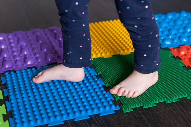 De benen van een klein kind op orthopedische matten. Heldere oppervlakken voor het lopen en vormen van de juiste boog van de voet. Massage puzzel mat. - Foto, afbeelding