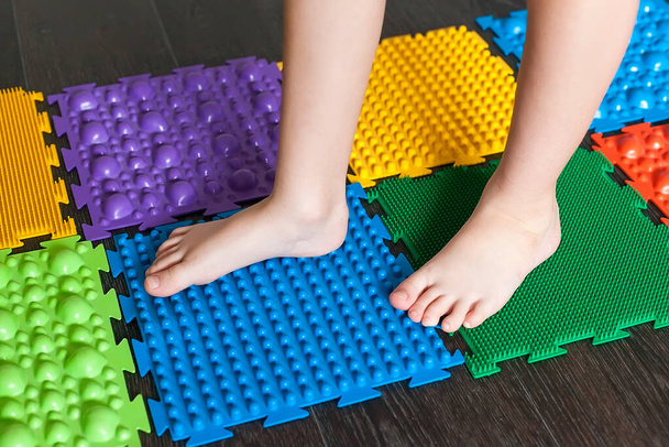Die Beine eines kleinen Kindes auf orthopädischen Matten. Helle Oberflächen zum Gehen und zur Bildung des richtigen Fußbogens. Massage-Puzzle-Matte. - Foto, Bild