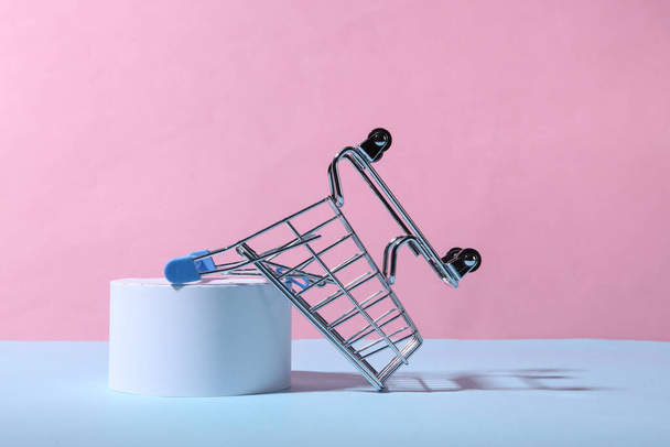 Mini shopping cart and podium on blue pink pastel background - Foto, afbeelding