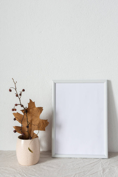 Décor intérieur mocap, cadre photo vide près du mur en béton peint blanc, branches avec feuilles sèches - Photo, image