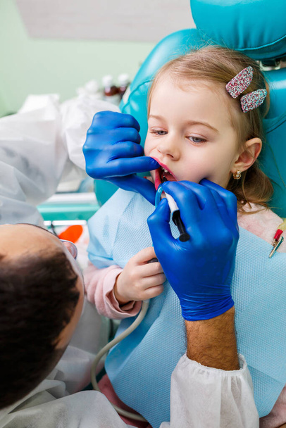 Egy hivatásos orvos, egy gyerekfogorvos, hangszerekkel kezeli egy kislány fogait. Fogászati rendelő vizsgálatra. A fogászati kezelés folyamata gyermekeknél - Fotó, kép