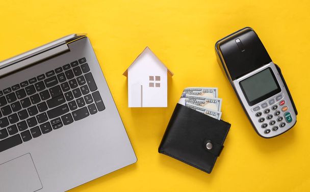 Koncepcja kupna domu. Laptop, mini dom, terminal płatniczy i torebka na żółtym tle. Widok z góry - Zdjęcie, obraz