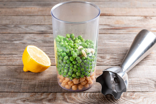 Guisantes verdes y garbanzos en un vaso con una licuadora. Haciendo hummus. Snack vegetariano - Foto, Imagen