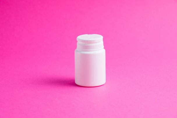 Белая банка с таблетками или витаминами на розовом бумажном фоне. Медицина на заднем плане с копировальным пространством - Фото, изображение