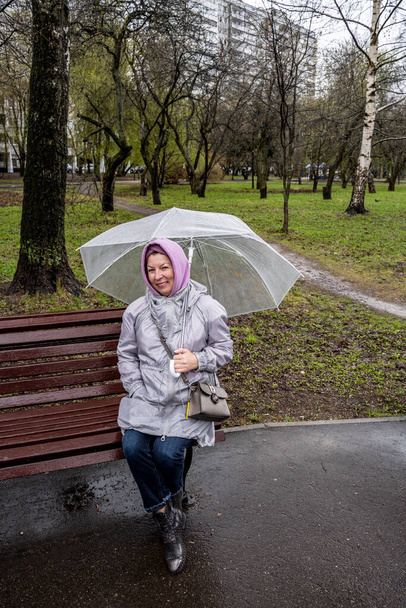женщина в плаще и с зонтиком гуляет по парку во время весеннего дождя  - Фото, изображение
