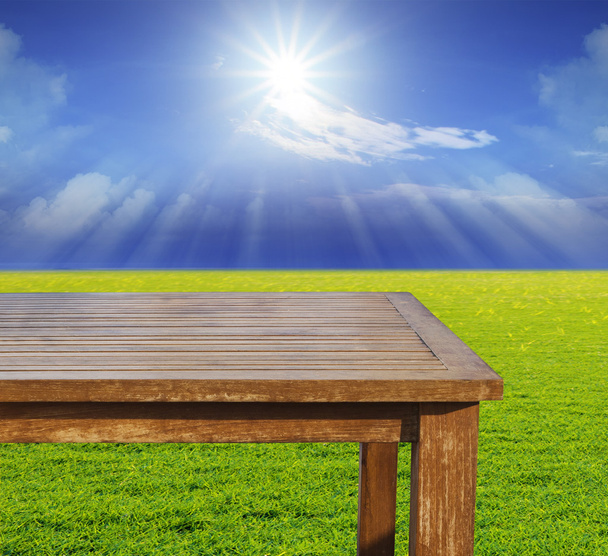 Пустое место верхний деревянный стол на зеленом травяном поле против солнца
 - Фото, изображение