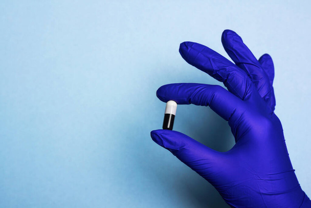 Pil capsule in de hand en medische handschoen op blauw - Foto, afbeelding