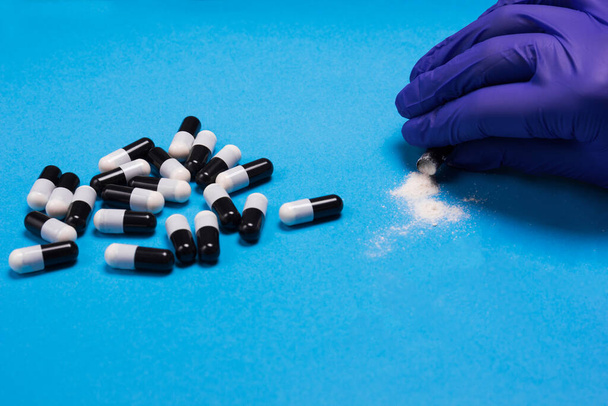 Pil capsule poeder in de hand en medische handschoen op blauw - Foto, afbeelding