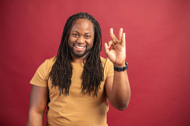 Cheerful African-American guy shows OK, isolated on red - Fotografie, Obrázek