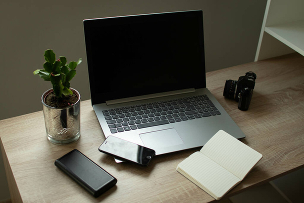 A laptop, an open notebook, a cellphone, and a plant on an office table - Фото, изображение