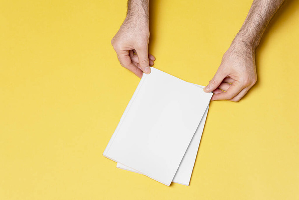 A male hand holding a closed book catalog with a blank cover on the yellow background, mock-up series template for design - Fotó, kép